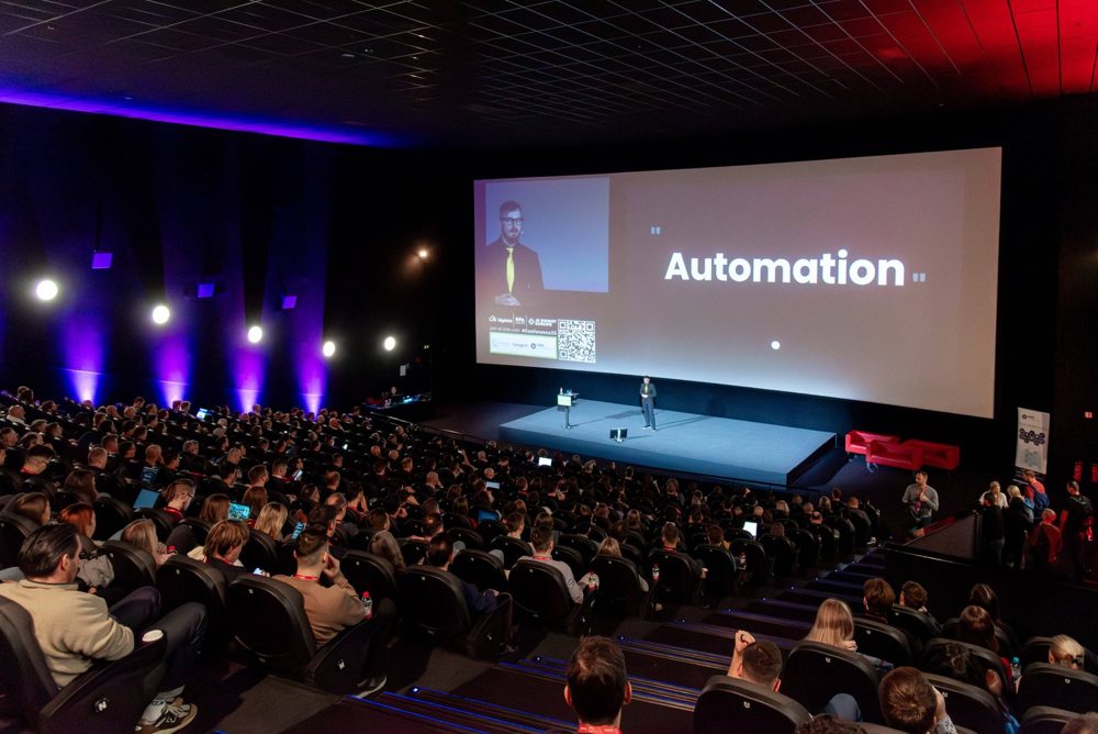 Full auditorium watching a talk on a cinema screen